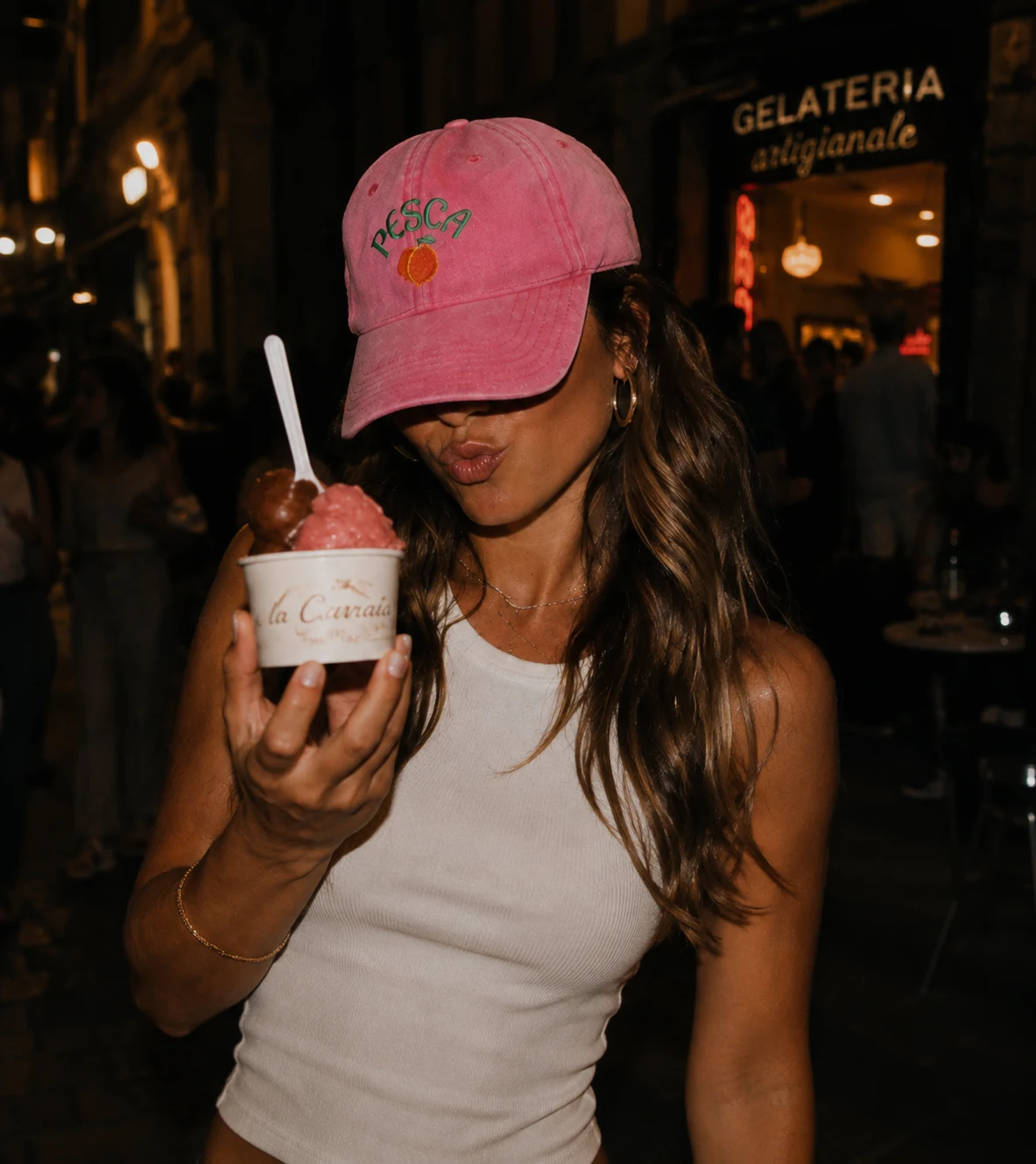 Two women with gelato at night, one wearing the pink Pesca cap