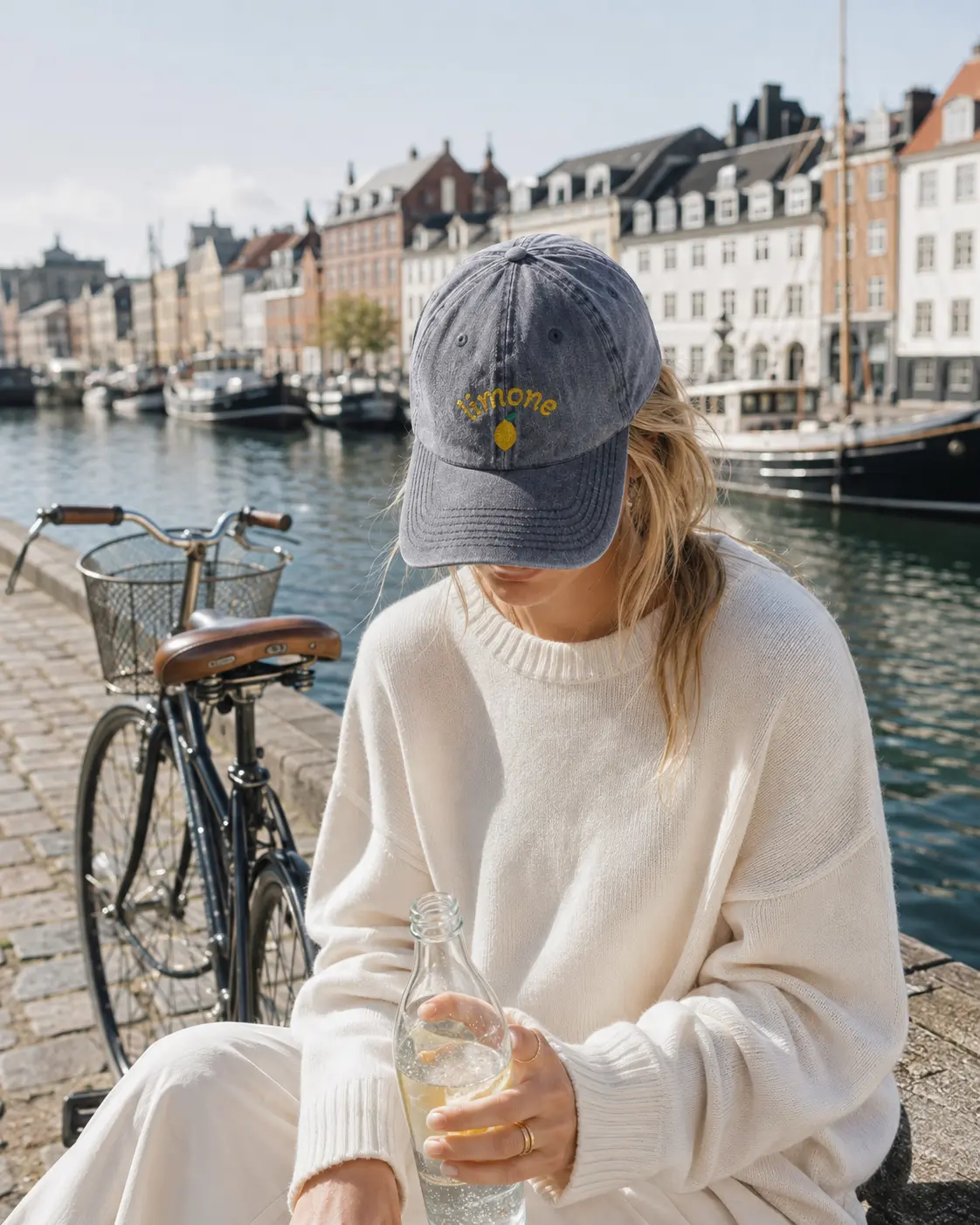 Woman wearing the Limone cap beside a harbour and a bicycle