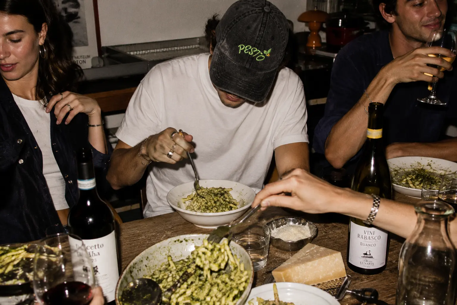 Friends sharing pesto pasta, one wearing the black Pesto cap