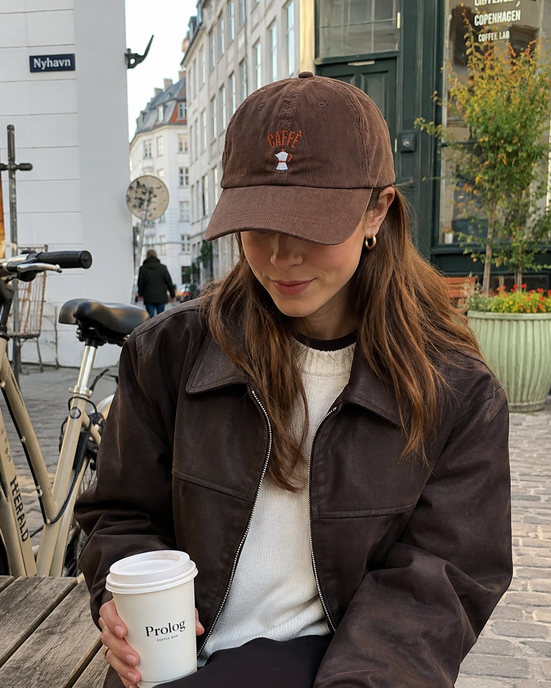 Woman wearing the brown Caffè cap outside a café with a takeaway coffee