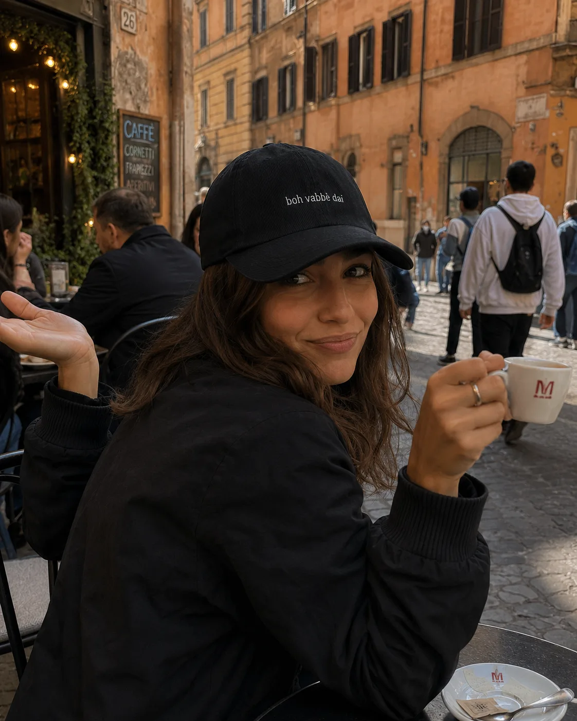 Woman wearing the black Boh Vabbè Dai cap at an Italian café with an espresso